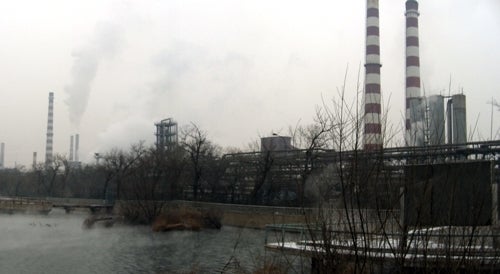 View across river, to smokestacks and bare trees.