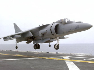 A harrier aircraft above a carrier flight deck.