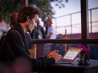 A curly-haired young man, with an earpiece hanging from his ear, types on a laptop.