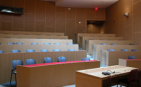 Photo of tiered tables and chairs with an instructor’s table at the front of the room. Modern wood paneling lines the walls.