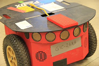 Red robot (approximately 6 inches tall with two wheels, and a flat top. A lego board is affixed to the top.