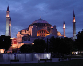 A night time view of an ornate structure with a rounded roof, framed by four pillars.