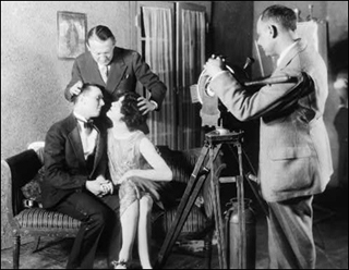 Two actors sitting on a couch with teacher directing a kissing scene.