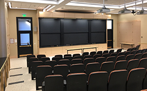 A view over several rows of tiered seats toward the chalkboards at the front of a lecture hall.