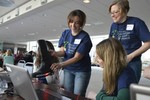 Three women are by a computer, holding a boot with wires attached to the computer.