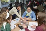 Girls are sitting around a table working on a project with electronic components.