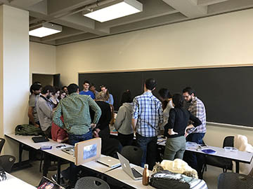 Students gathered in a group in a classroom watching a student project demo.